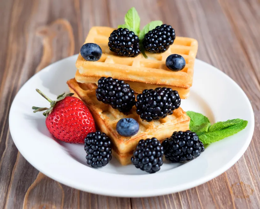 Waffles stacked on a plate with blackberries, blueberries and a strawberry
