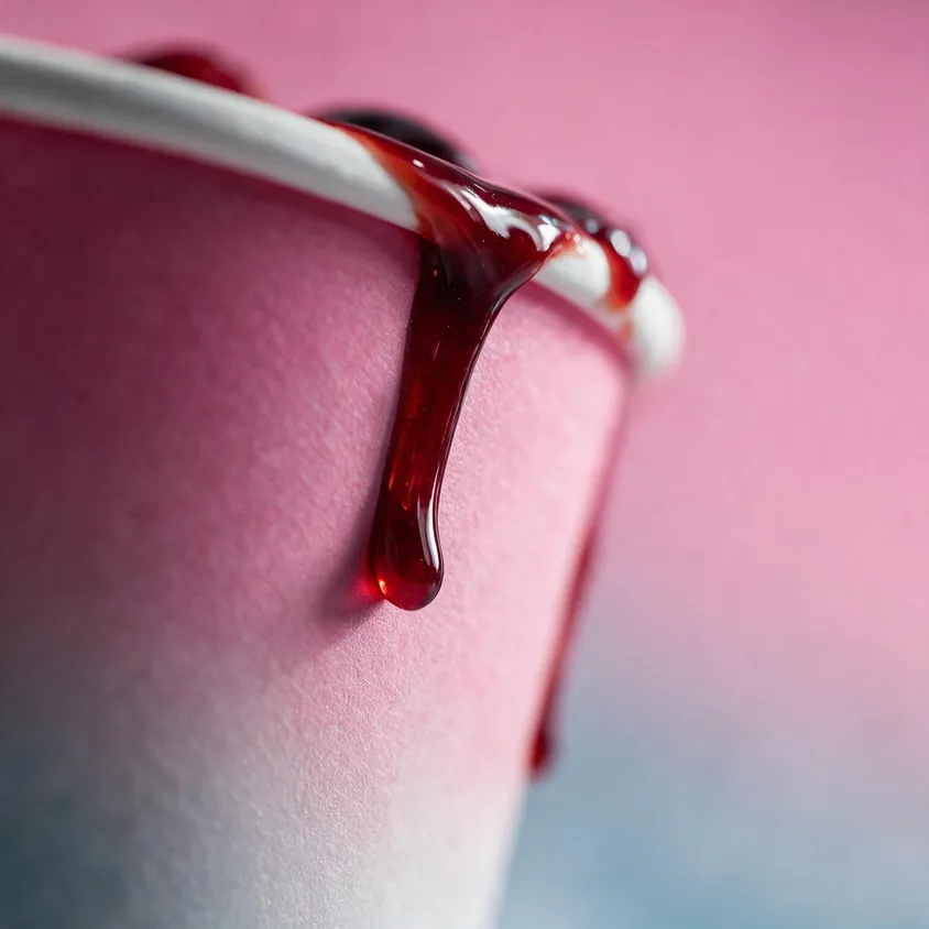 Glossy cherry sauce dripping down the side of a pink takeaway tub, close up